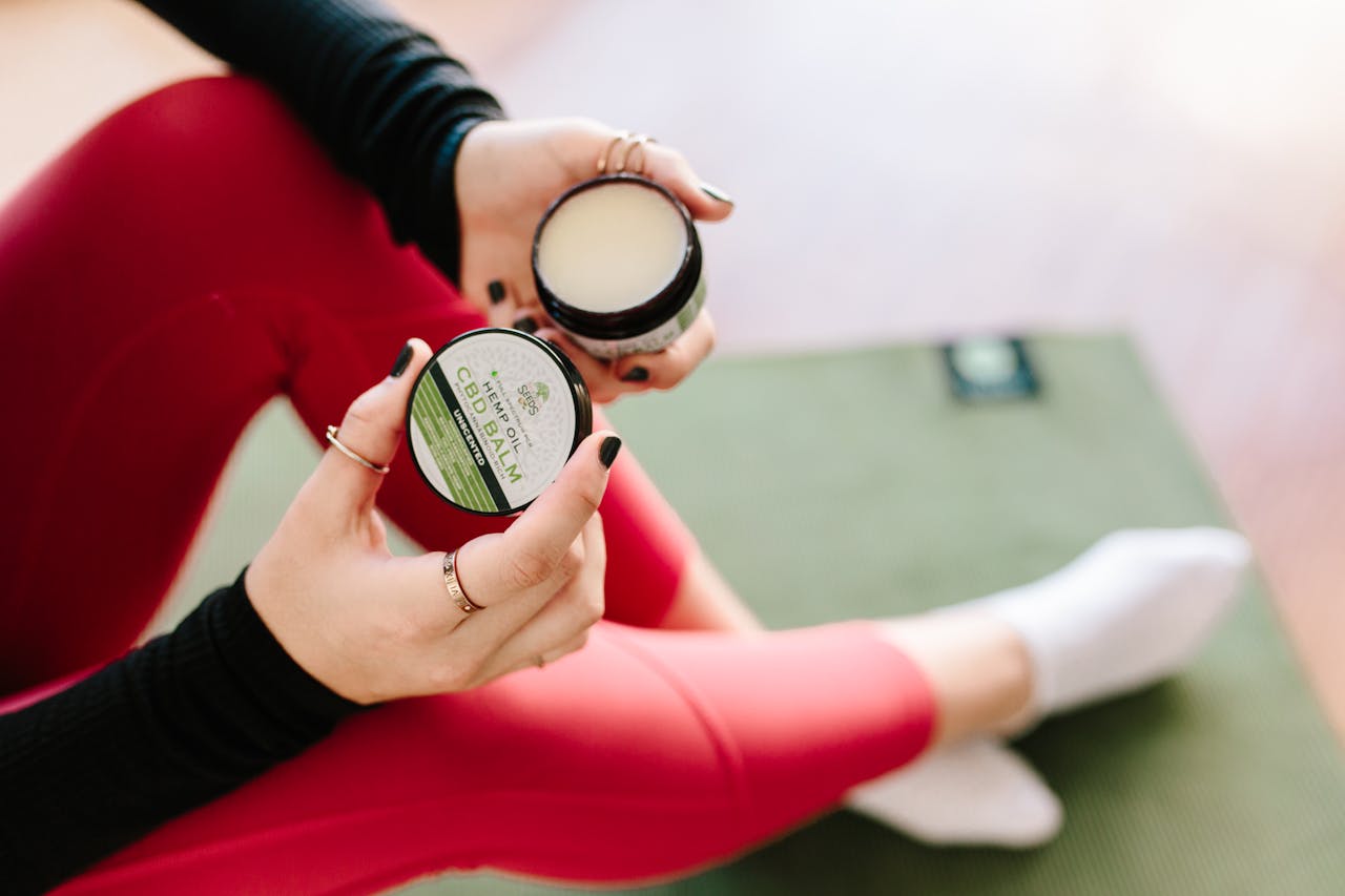 Close-up of a woman holding CBD balm while seated on a yoga mat, showcasing wellness.