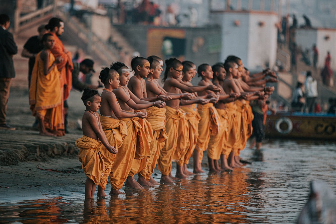 A group of young monks in orange robes perform a ritual by the Ganges River in Varanasi, India.